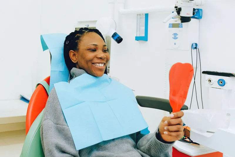 A smiling woman in the dental chair checking her teeth in a hand mirror
