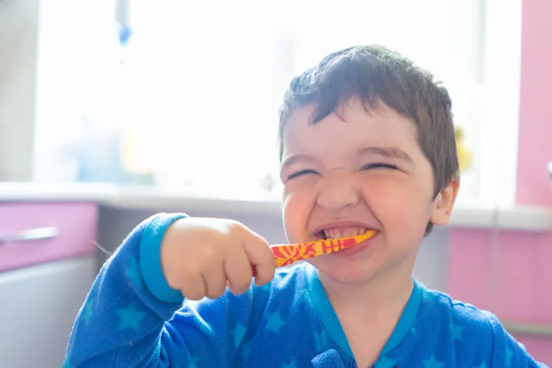 A young boy in pyjamas grinning as he brushes his teeth