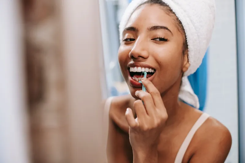 A smiling woman cleaning between her teeth with a floss pick