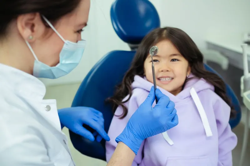 A smiling girl in the dental chair while the dentist shows her a small mirror