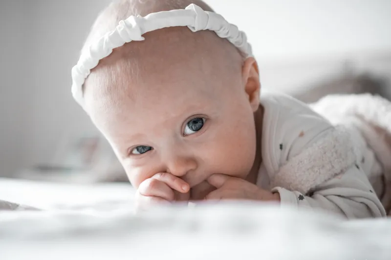 A baby lying on a soft blanket with her fingers in her mouth
